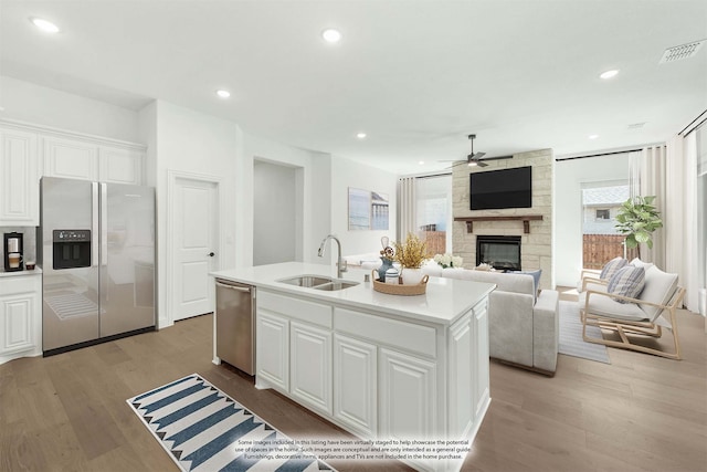 kitchen with an island with sink, sink, white cabinetry, appliances with stainless steel finishes, and a fireplace