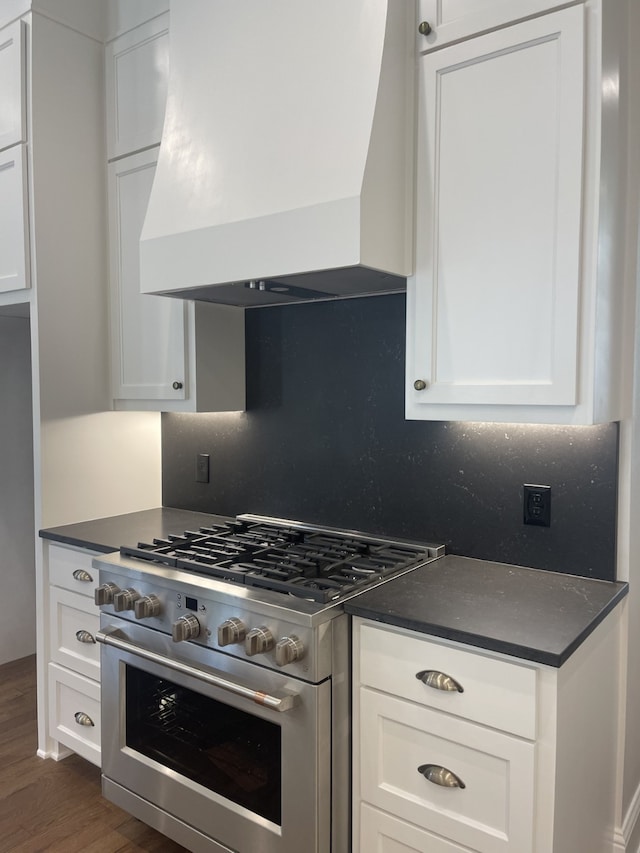 kitchen with custom exhaust hood, stainless steel range, white cabinetry, and dark countertops