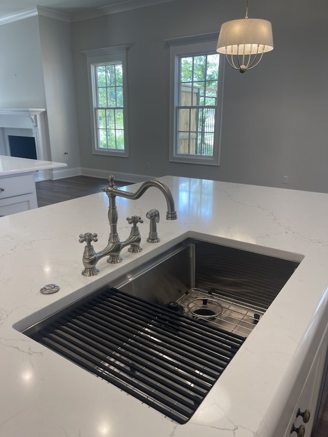 interior details featuring crown molding, light stone counters, hanging light fixtures, white cabinets, and a sink