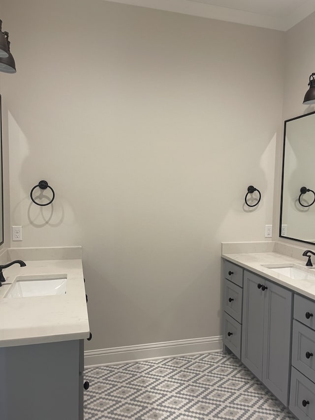 bathroom with crown molding, two vanities, baseboards, and a sink