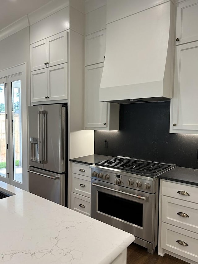 kitchen featuring premium appliances, white cabinetry, decorative backsplash, and premium range hood