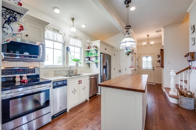 kitchen with decorative light fixtures, appliances with stainless steel finishes, butcher block countertops, crown molding, and dark wood-type flooring