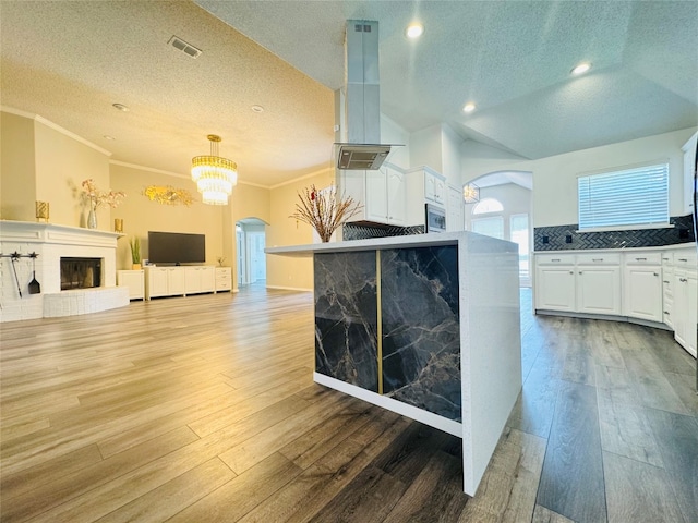 kitchen with ornamental molding, wood-type flooring, a brick fireplace, and white cabinetry