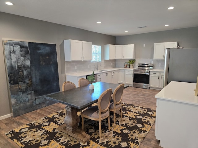 kitchen with white cabinets, sink, light hardwood / wood-style floors, tasteful backsplash, and stainless steel appliances