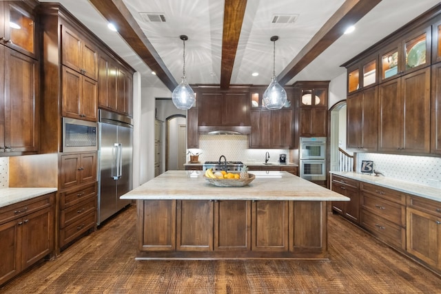 kitchen featuring built in appliances, a center island, beamed ceiling, and hanging light fixtures