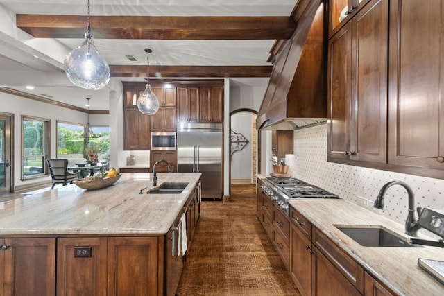 kitchen featuring a center island with sink, light stone counters, built in appliances, and sink