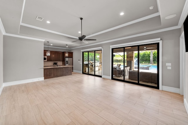 unfurnished living room with ceiling fan, a raised ceiling, ornamental molding, and sink