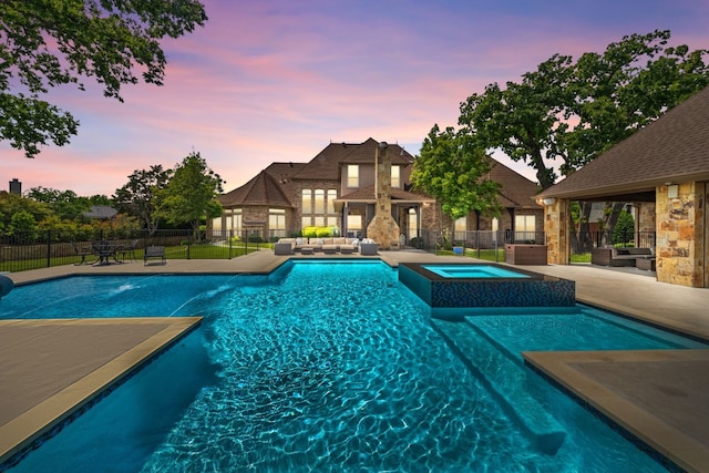 pool at dusk featuring an outdoor living space, a patio area, and an in ground hot tub