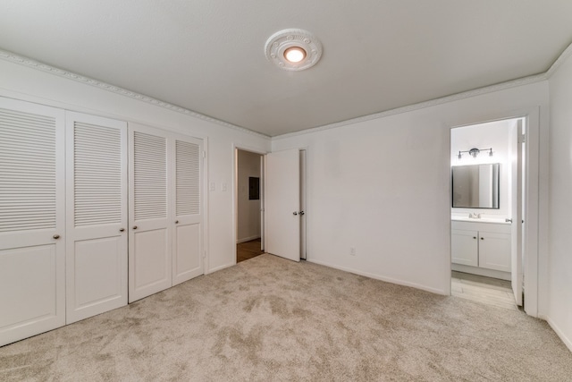 unfurnished bedroom with ornamental molding, light colored carpet, and ensuite bath