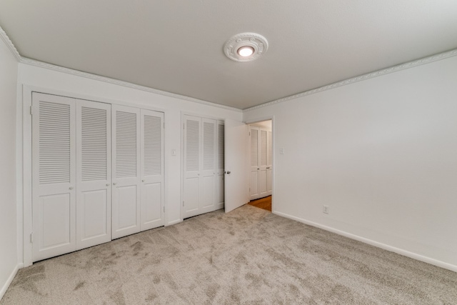 unfurnished bedroom with multiple closets, crown molding, and light carpet