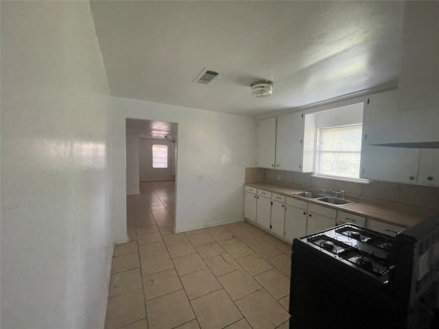 kitchen featuring sink, black range, white cabinetry, and light tile floors