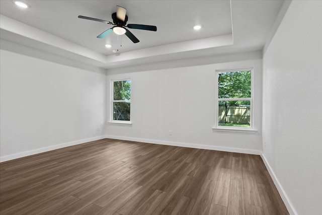 unfurnished room featuring hardwood / wood-style flooring, a healthy amount of sunlight, a raised ceiling, and ceiling fan