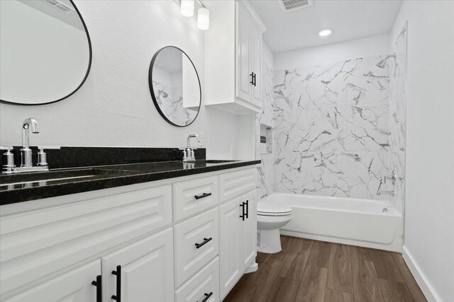 full bathroom featuring wood-type flooring, tiled shower / bath combo, double sink vanity, and toilet