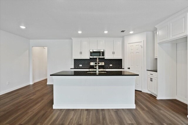 kitchen with backsplash, white cabinets, a center island with sink, and dark wood-type flooring