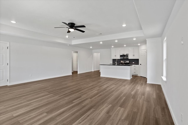 unfurnished living room featuring hardwood / wood-style flooring, a raised ceiling, sink, and ceiling fan