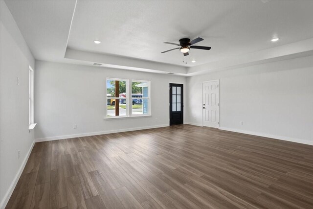 unfurnished living room featuring a raised ceiling, ceiling fan, and hardwood / wood-style floors