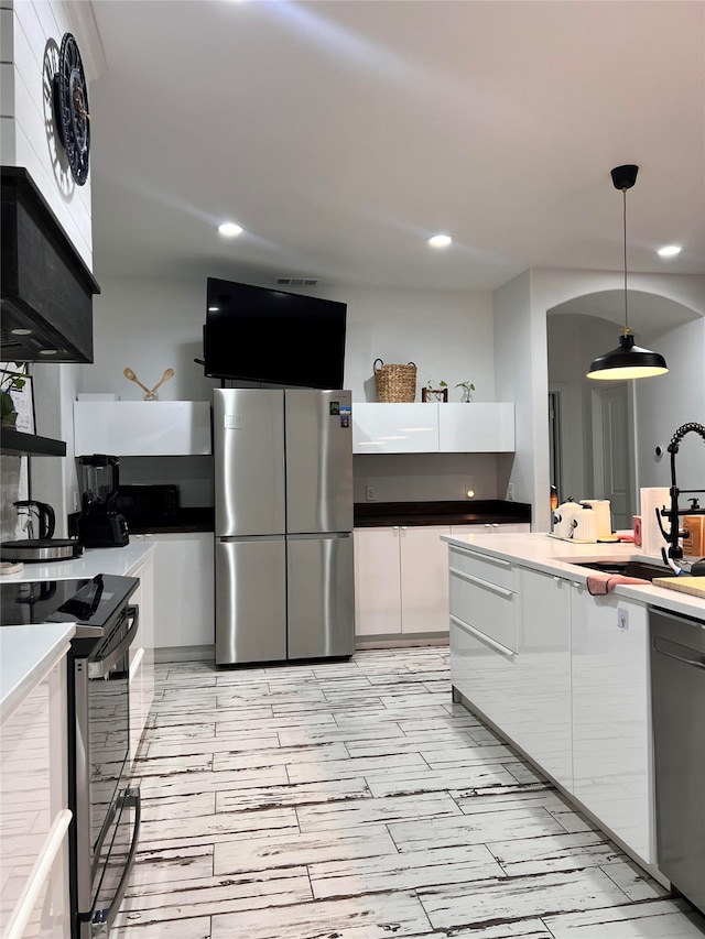 kitchen with hanging light fixtures, white cabinetry, appliances with stainless steel finishes, exhaust hood, and sink