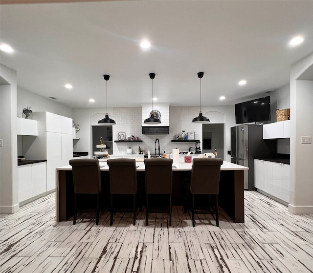 kitchen with a breakfast bar, a large island with sink, white cabinetry, and tasteful backsplash