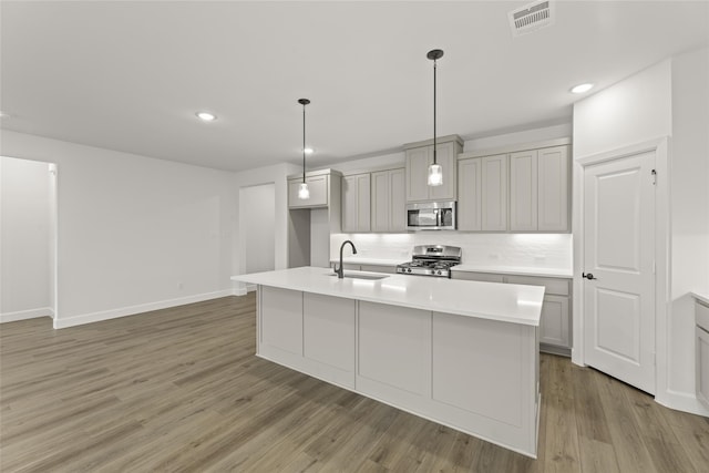 kitchen with appliances with stainless steel finishes, sink, decorative light fixtures, hardwood / wood-style floors, and an island with sink