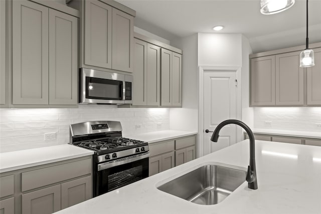 kitchen with gray cabinetry, sink, tasteful backsplash, decorative light fixtures, and appliances with stainless steel finishes