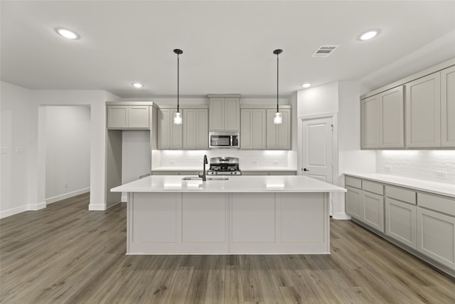 kitchen featuring dark wood-type flooring, a kitchen island with sink, pendant lighting, and stainless steel appliances