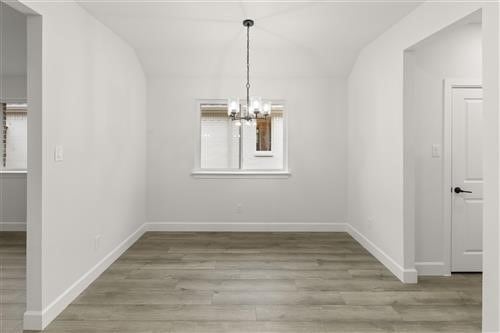 unfurnished dining area featuring a notable chandelier, a healthy amount of sunlight, vaulted ceiling, and light wood-type flooring