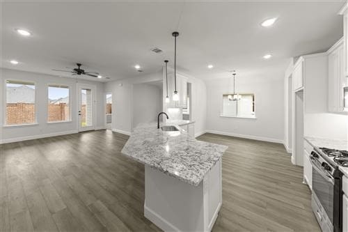 kitchen with dark hardwood / wood-style flooring, stainless steel gas range, decorative light fixtures, a center island with sink, and white cabinets