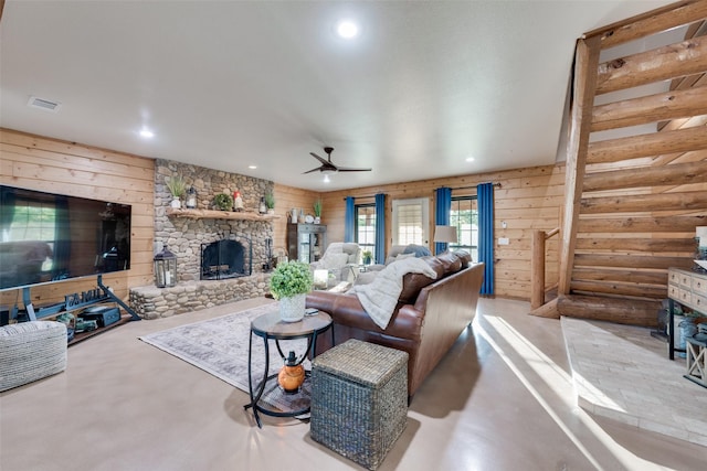 living room featuring a stone fireplace, wooden walls, concrete floors, and ceiling fan