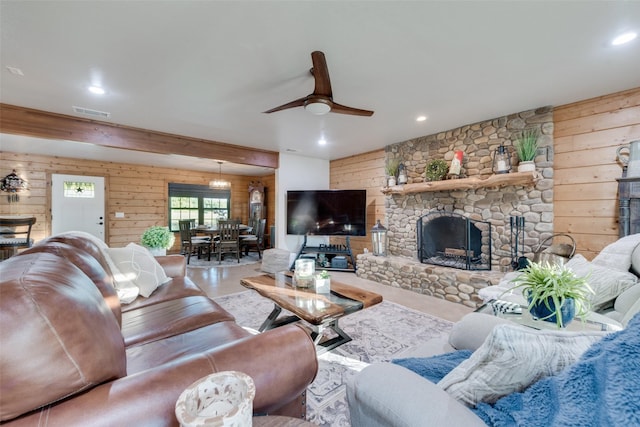 living room featuring a stone fireplace, wooden walls, and ceiling fan