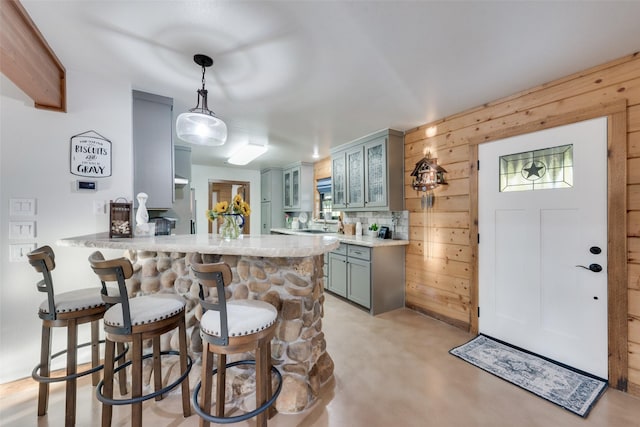 kitchen featuring a breakfast bar, kitchen peninsula, wood walls, and decorative light fixtures