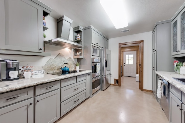 kitchen featuring wall chimney exhaust hood, appliances with stainless steel finishes, gray cabinets, and light stone countertops