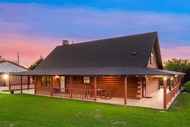 back house at dusk featuring a patio area and a lawn