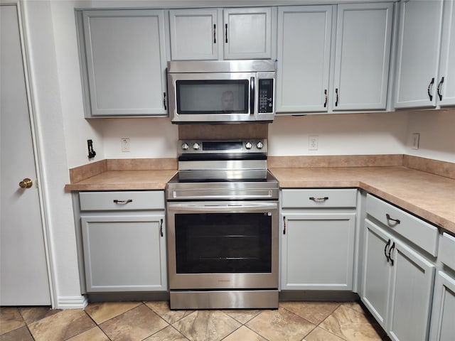 kitchen featuring gray cabinetry, light tile floors, and appliances with stainless steel finishes