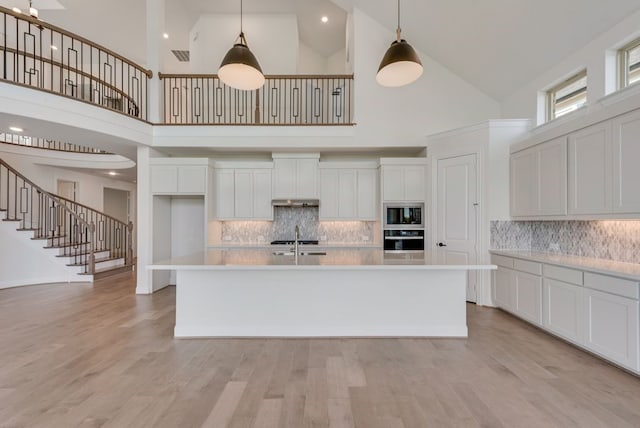 kitchen with light wood-type flooring, stainless steel appliances, high vaulted ceiling, and a center island with sink