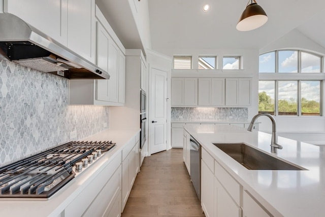 kitchen featuring wall chimney range hood, sink, hanging light fixtures, decorative backsplash, and stainless steel appliances