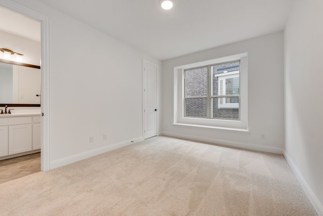 unfurnished bedroom with ensuite bathroom, light colored carpet, and sink