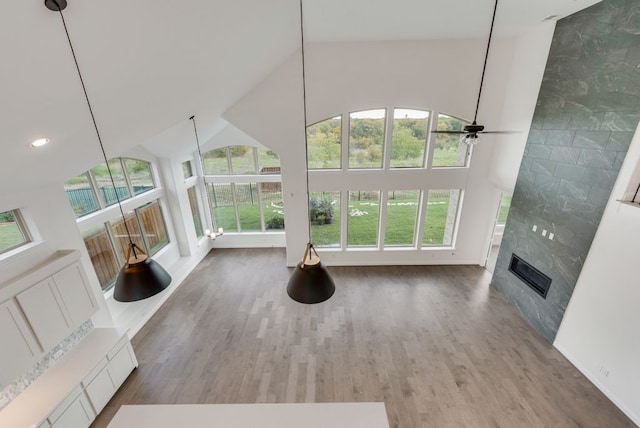 unfurnished living room with hardwood / wood-style flooring, plenty of natural light, a high ceiling, and a tiled fireplace