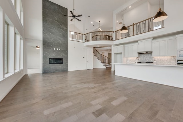 unfurnished living room with sink, light wood-type flooring, a fireplace, and high vaulted ceiling