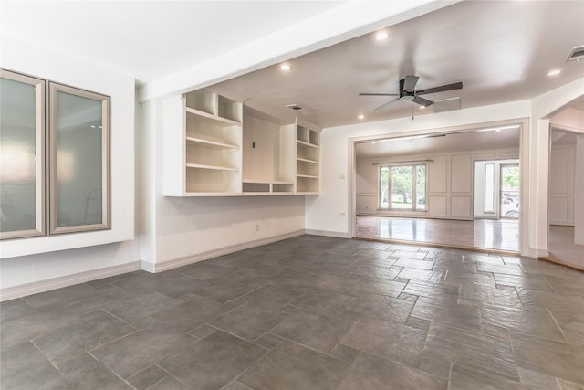 unfurnished living room featuring built in features, dark tile flooring, and ceiling fan