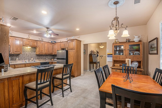 kitchen with decorative light fixtures, ceiling fan with notable chandelier, light colored carpet, backsplash, and stainless steel refrigerator