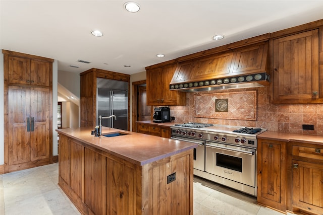 kitchen featuring premium range hood, a kitchen island with sink, sink, decorative backsplash, and premium appliances