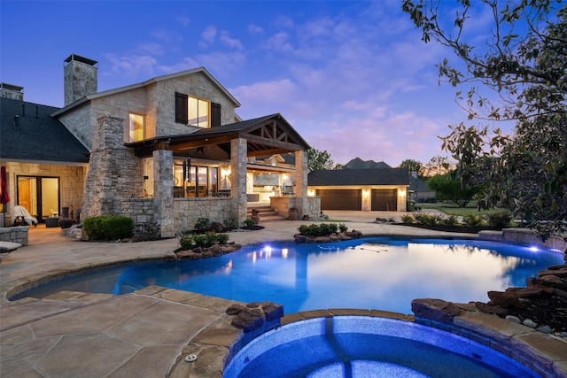 pool at dusk with an in ground hot tub and a patio