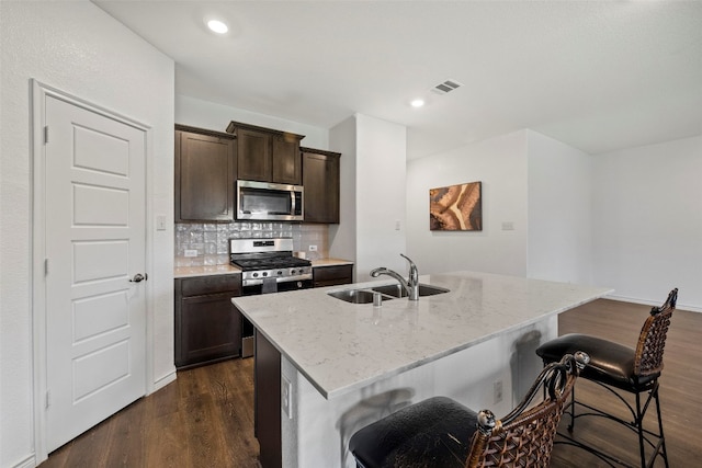 kitchen featuring backsplash, stainless steel appliances, dark wood-type flooring, a kitchen island with sink, and sink