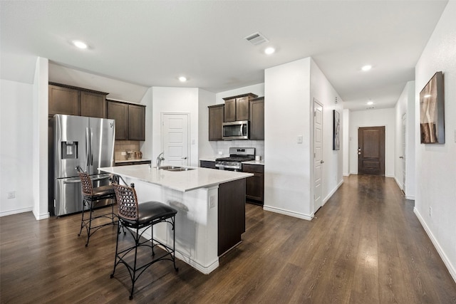 kitchen featuring backsplash, appliances with stainless steel finishes, dark wood-type flooring, and an island with sink