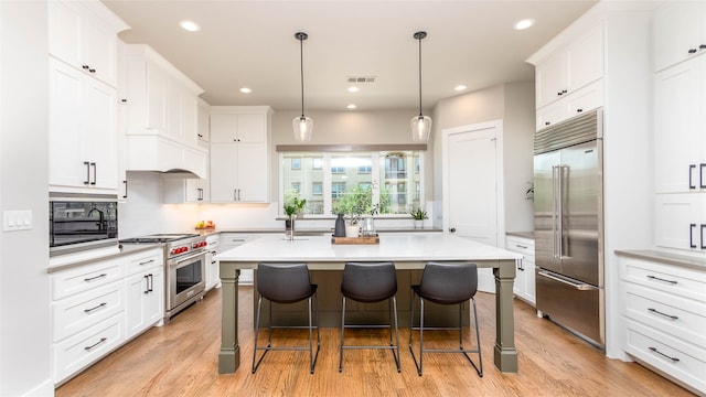 kitchen featuring light hardwood / wood-style floors, a kitchen island with sink, built in appliances, and white cabinetry