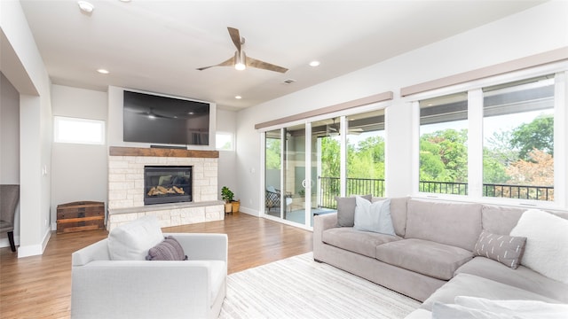 living room featuring light hardwood / wood-style floors, ceiling fan, and a stone fireplace