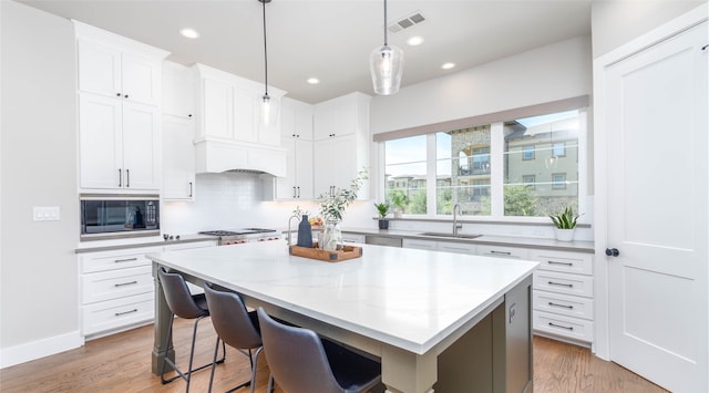 kitchen featuring white cabinets, black microwave, a center island, decorative light fixtures, and sink