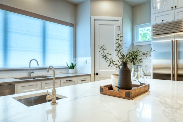 kitchen featuring white cabinets, sink, stainless steel appliances, light stone countertops, and decorative backsplash