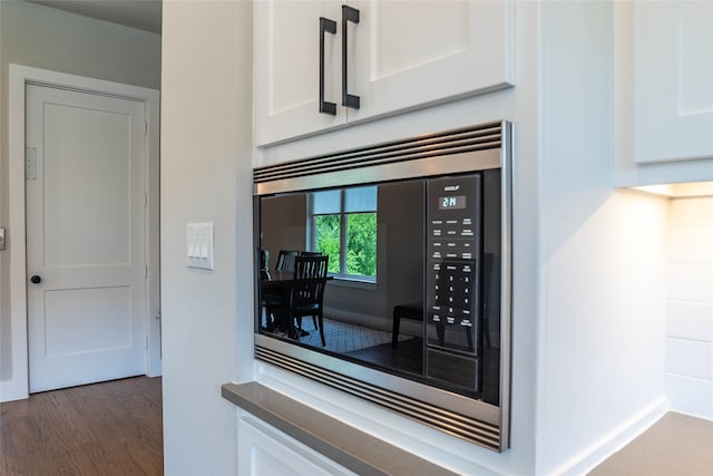 interior details featuring white cabinets, stainless steel microwave, and dark wood-type flooring