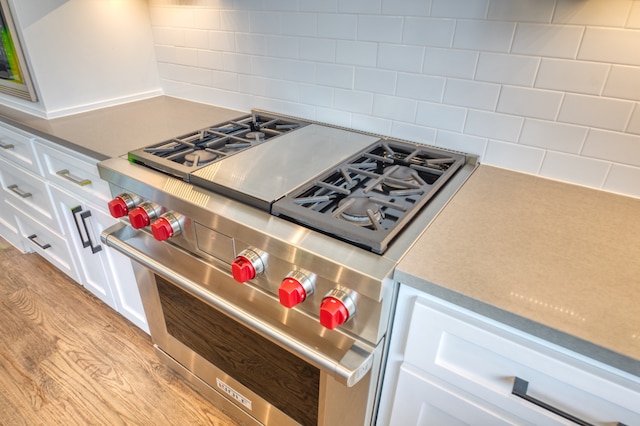 kitchen with double oven range, tasteful backsplash, light wood-type flooring, and white cabinets